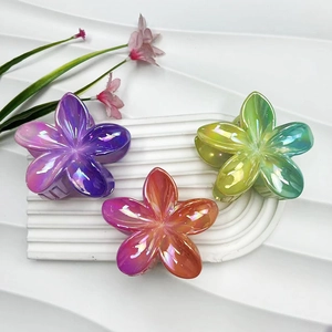 Close-up of three gradient frangipani hair claws with iridescent finish on white texture