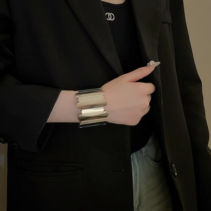 Macro detail of a wide silver wavy metal cuff bracelet worn against a black suit sleeve