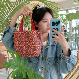 Close-up of small floral corduroy tote bag with red handles in a cozy cafe setting
