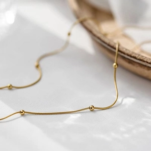 Detail of gold snake bone chain necklace with small beads on white textured fabric