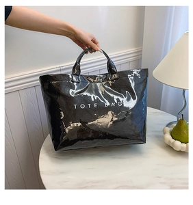 Detail of black glossy tote bag with crinkle texture and white printed logo on marble table