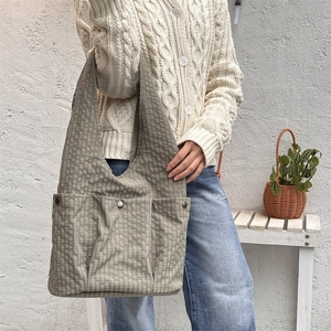 Detail of taupe checkered tote bag with two large front pockets and metallic studs