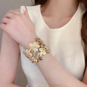 Detailed view of wide gold metal cuff bracelet with 3D floral petal design on arm