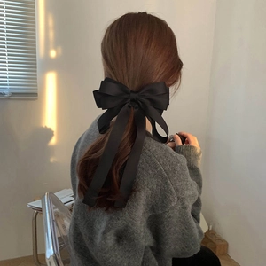 Detail of a large black satin bow hair clip worn on the back of the head by a model