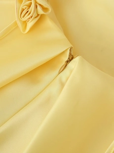 Macro detail of a yellow satin dress featuring an invisible zipper and a 3D floral decoration