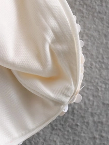 Detail of sequined bow decoration and fine knitted texture on cream-colored jacket