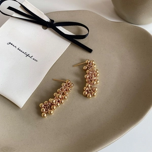 Detail shot of cluster beaded gold drop earrings on a ceramic jewelry tray