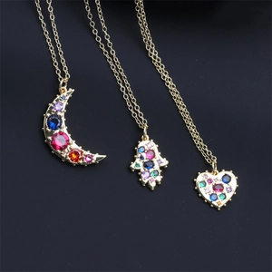 Close-up of golden necklaces with Hamsa, moon and heart pendants set with colorful crystals