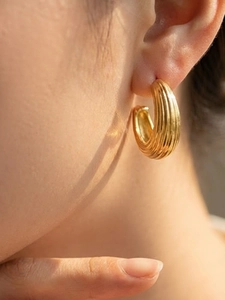 Gros plan de boucles d'oreilles créoles torsadées plaquées or 18 carats sur un mannequin