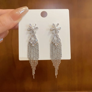 Close-up of tassel earrings with crystals and imitation pearls held on white cardstock