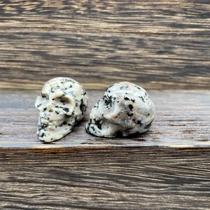 Macro shot of two carved dalmatian jasper crystal skulls on a dark wooden surface