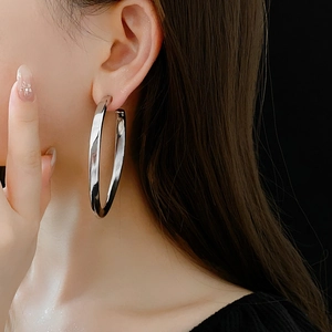 Macro detail of oversized silver oval hoop earrings with high-polish metallic finish