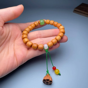 Detail of wooden bead bracelet with green jade beads and a carved lotus seed pod charm