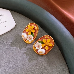 Macro shot of vintage oval floral earrings with red enamel, pearl, and gold finish
