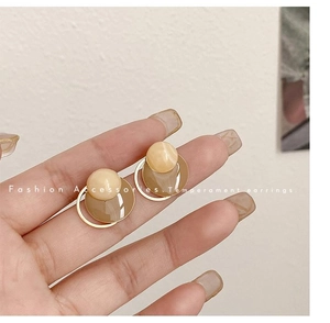 Close-up of elegant amber-toned geometric earrings with golden metallic frames held by hand