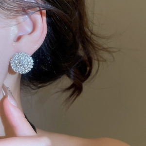 Close-up of a model wearing a luxurious round diamond-studded earring with elegant lighting