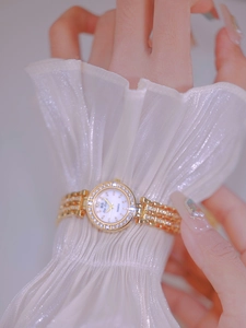 Detailed shot of a gold crystal watch with pearl dial worn on a female wrist