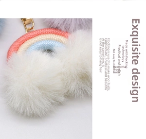 Close-up of rainbow woven keychain with large white fluffy pompoms and gold metal clasp