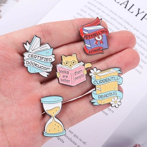 Hand holding five metal enamel bookworm pins featuring magical cat and reading slogans