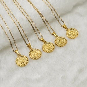 Collier en acier doré avec pendentifs lettres en relief sur un tissu blanc moelleux