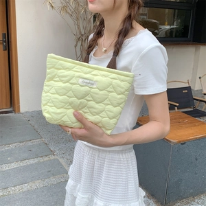Outdoor lifestyle shot of a pale yellow quilted heart clutch bag with a zipper closure
