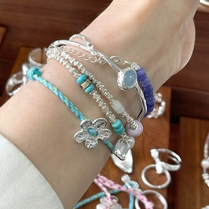Close-up of layered blue beaded bracelets and S925 silver flower charm on female wrist