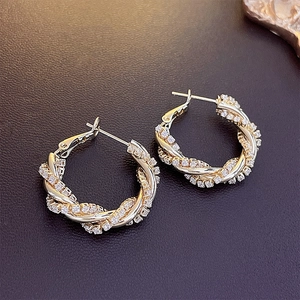 Detail shot of golden twisted hoop earrings with zircon stones on a dark background