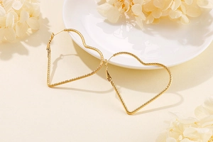 Detail view of large gold heart hoop earrings with textured twisted rope pattern design