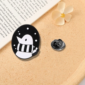 Cartoon penguin enamel pin with striped scarf and silver clutch back on vintage book background
