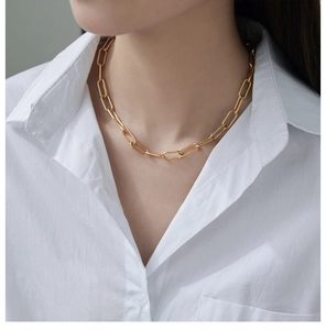 Close-up of a minimalist chunky gold paperclip chain necklace worn on a white shirt