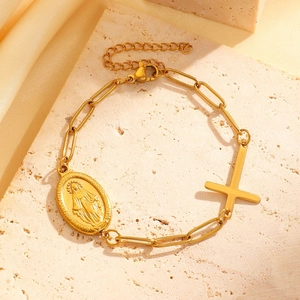 Detail of gold paperclip chain bracelet with Virgin Mary medal and cross pendant on stone
