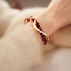 Detail of gold-plated wavy metal and dark red resin bangle on a cream sweater