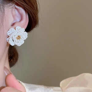 Close-up of camellia pearl beaded earrings with golden stamens worn on an ear