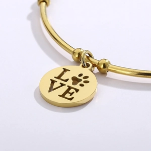 Gold stainless steel open bangle featuring a round LOVE charm with a pet paw print motif