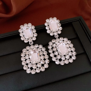Macro shot of silver crystal flower earrings with rectangular rhinestones on silk fabric