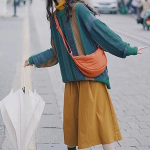 Orange nylon crescent crossbody bag styled with a colorful striped knit sweater and skirt