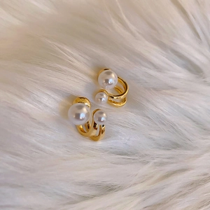 Macro detail of gold C-shape pearl earrings with double-layered curve on plush background