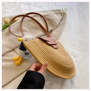 Detail of semi-circle straw woven shoulder bag with brown leather strap and duck charm