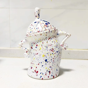 Detail of white ceramic canister with colorful splatter pattern and lid on white table