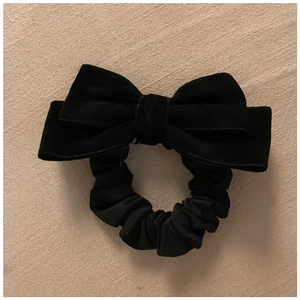 Detailed close-up of a black velvet bow hair tie on a soft beige fabric surface