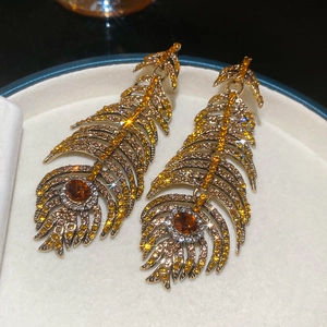Detailed close-up of luxury gold feather earrings with amber and yellow rhinestones