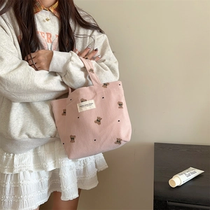 Detail of pink corduroy handbag with bear embroidery held by a model in casual outfit