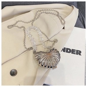 Detail of silver shell mini bag with metal beads and clear bead chain on beige suit
