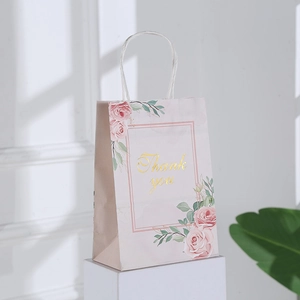 Detailed view of pink floral gift bag with gold Thank You text on white display stand