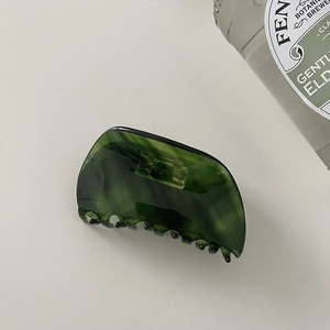 Top view of a dark green tortoiseshell acetate claw clip on a clean white background