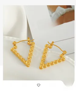 Detail of gold beaded V-shaped earrings with metallic granules on white ceramic