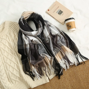 Close-up of black and white plaid scarf with long tassels on a knitted sweater