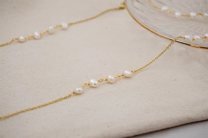 Detailed close-up of a long gold layered necklace with white baroque freshwater pearls