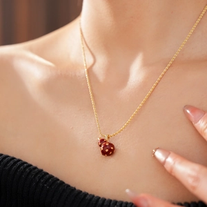 Close-up of a model wearing a gold 18k plated necklace with a red enamel gourd pendant