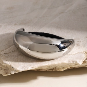 Minimalist silver curved metal ponytail cuff displayed on a natural stone background